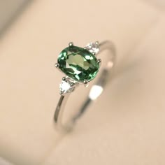 This ring features a (6*8 mm oval cut green sapphire). Customization is available. It is made by hand, and it will take about 7 days to finish the ring after your payment is completed. Main stone: 6*8mm oval cut Main stone weight:1.75ct Metal type: sterling silver finished with rhodium/14k gold Accent stone: cz Customization is available, I also can make it with 14k solid gold (white or yellow or rose) and diamond accent stone, just feel free to contact me. Any question, just let me know. :) My Green Diamond Ring Silver, Silver Rings With Green Stones, Blue Green Sapphire Engagement Ring White Gold, Green Stone Ring Silver, Silver Green Engagement Ring, Green Diamond Ring Engagement, Sapphire Green Engagement Ring, Silver And Green Wedding Ring, Silver Ring With Green Stone