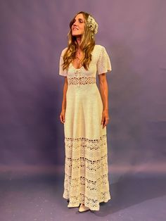 a woman wearing a white dress and flower in her hair standing against a purple background