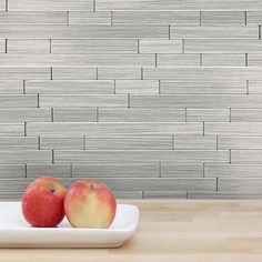 two apples are sitting on a plate in front of a gray brick wall behind them