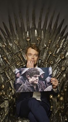 a man sitting on the iron throne holding up a photo