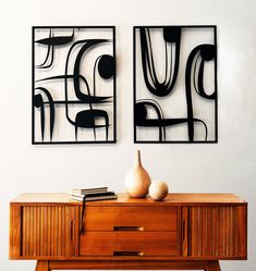 two black and white art pieces hanging on the wall above a wooden table with a vase