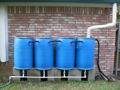 three large blue barrels sitting in front of a brick building with a hose attached to them