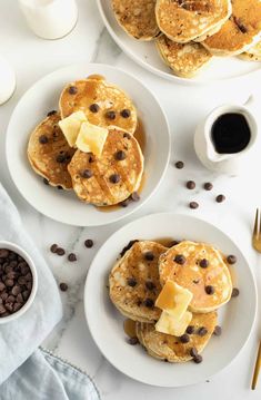 pancakes with butter and chocolate chips on white plates next to coffee, milk and spoons