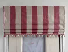 a red and white striped roman blind with tassels on the top, in front of a window