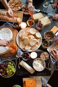 people are gathered around a table with cheeses, crackers and other food items