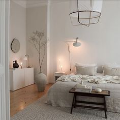 a bedroom with white walls and flooring has a large bed in the middle, surrounded by candles