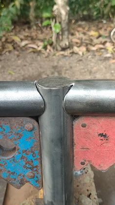 an old metal fence with red and blue paint peeling off the sides, in front of some trees