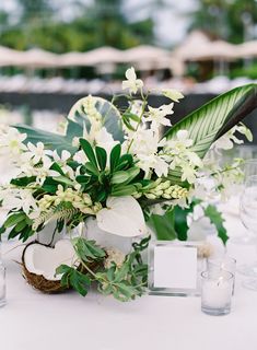 an arrangement of flowers and greenery on a white table cloth with place cards in the center