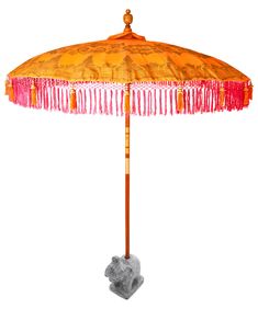 an orange umbrella with fringes on it is next to a gray rock and a white background