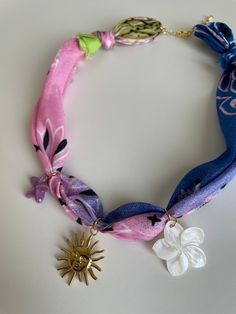 a necklace with flowers and a sun charm on it's end, sitting on a white surface