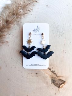 the bat earrings are on display in front of a feathery background, and it's black with gold accents