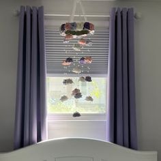 a white bed sitting under a window next to a purple drapes and curtain valance