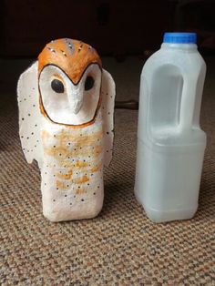 an owl figurine next to a bottle of milk on the floor in front of a carpeted area