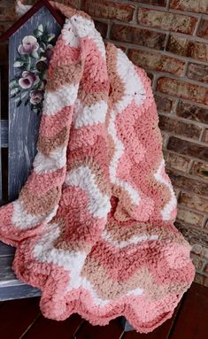 a pink and white blanket sitting on top of a wooden chair next to a brick wall