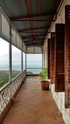 an empty porch overlooking the ocean with shutters on both sides and potted plants