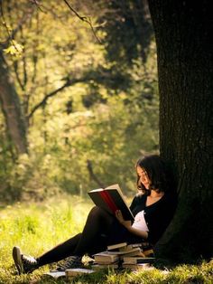 a woman sitting under a tree reading a book