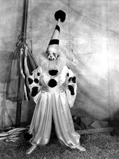 a man dressed up as a clown with his hands in the air while standing next to a pole