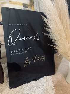 a welcome sign sitting on top of a rug next to a vase filled with dry grass