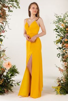 a woman wearing a yellow dress standing in front of flowers