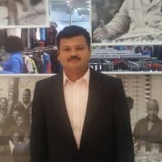 a man standing in front of a wall with pictures on it and wearing a suit