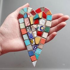 a hand holding a heart shaped mosaic piece