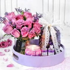 a bouquet of pink roses in a purple container with candles and perfumes on a table