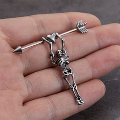 a hand holding a silver pin with a skeleton on it's back and an arrow in the middle