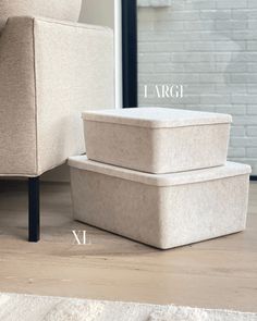 two storage boxes sitting on the floor next to a chair and rug in front of a brick wall