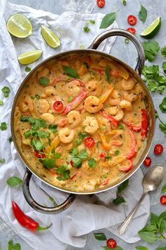 a pan filled with shrimp and vegetables on top of a table next to spoons