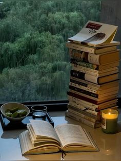 a stack of books sitting on top of a table next to a window