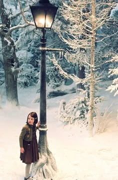 a woman standing next to a lamp post in the snow