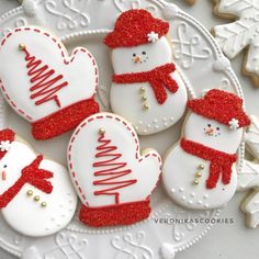 four decorated cookies on a plate with snowmen and christmas trees in the shape of hearts