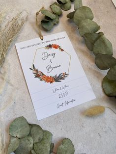 the wedding stationery is laid out with eucalyptus leaves and dried flowers on it's table