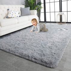 a baby crawls on the floor in front of a white couch and gray rug