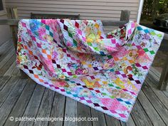 a multicolored quilt sitting on top of a wooden deck next to a house