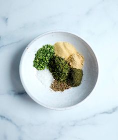 three different types of spices in a white bowl on a marble countertop, including green and yellow