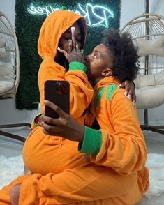 two people in orange onesuits sitting on the floor and one is holding a cell phone