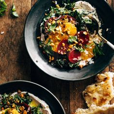 two black bowls filled with food on top of a wooden table next to bread and vegetables