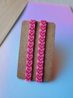 two pink and white bracelets sitting on top of a piece of cardboard next to each other