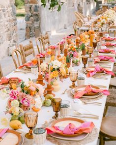 a long table is set with orange and pink flowers, plates and utensils