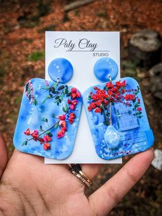 a pair of blue earrings with red flowers on the front and back of them, sitting in someone's hand