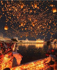 many people are sitting on the ground with lanterns floating in the air above them at night