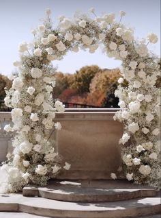 a white wedding arch decorated with flowers and greenery