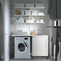 a washer sitting next to a dryer in a room with white tile on the walls