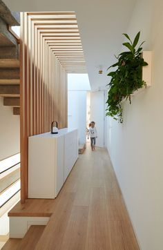 a woman walking down a hallway next to a plant hanging from the ceiling above her head