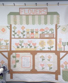 a quilted wall hanging on the side of a building with flowers written on it