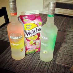 three bottles of alcohol sitting on top of a table next to two bags of chips