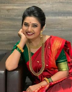 a woman in a red and green sari sitting on a couch with her hand under her chin