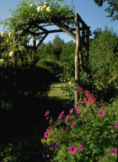 an arbor with flowers in the foreground and trees in the background