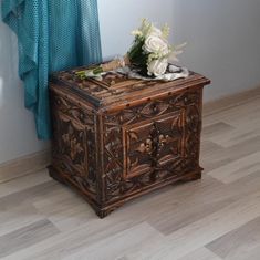 an ornate wooden box with flowers on top sits in front of a curtained window